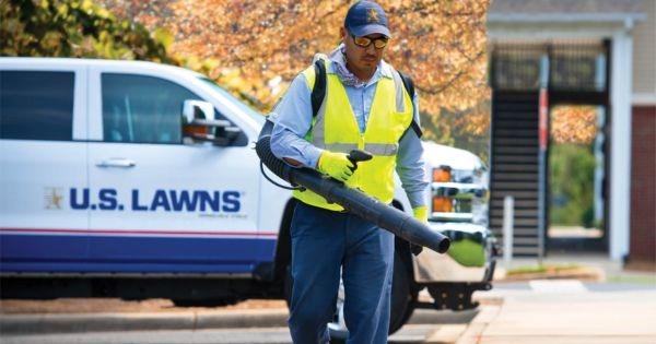 U.S. Lawns landscaping technician performing commercial property maintenance service beside branded company truck