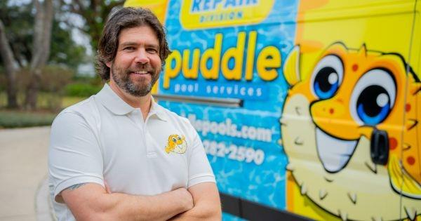 Puddle Pools franchise owner standing beside branded pool service van, highlighting pool maintenance services in CA