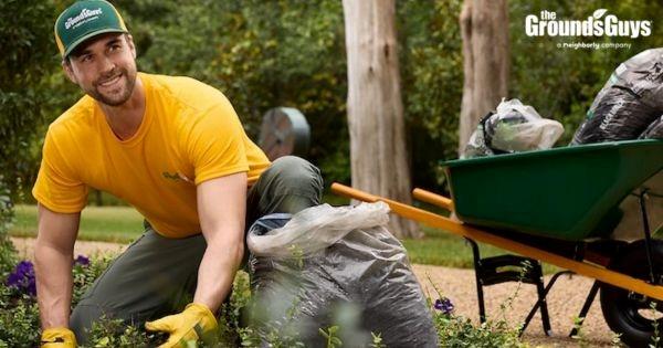 The Grounds Guys franchise landscaping professional performing yard cleanup, highlighting lawn care and grounds maintenance