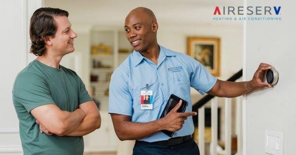 Aire Serv franchise HVAC technician assisting homeowner with thermostat, highlighting heating and air conditioning services