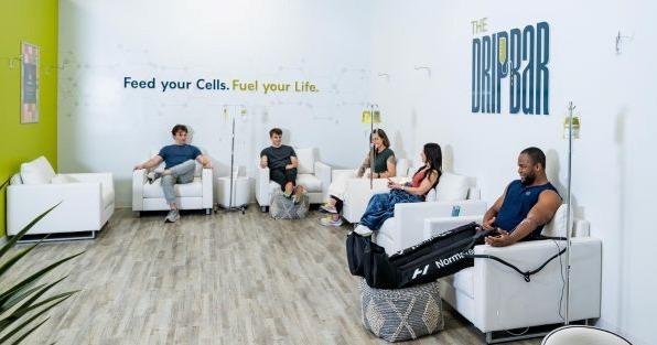 The DRIPBaR wellness franchise featuring clients receiving IV vitamin therapy in a modern lounge focused on cellular health and wellness.