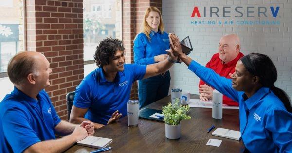 Aire Serv franchise team celebrates a new owner's journey with a high-five, highlighting teamwork and success in the HVAC industry.